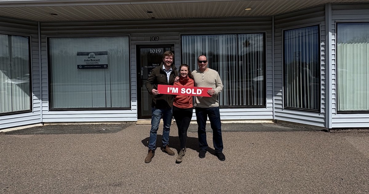New owners holding an &ldquo;I&rsquo;m Sold&rdquo; sign in front of a brick rental property
